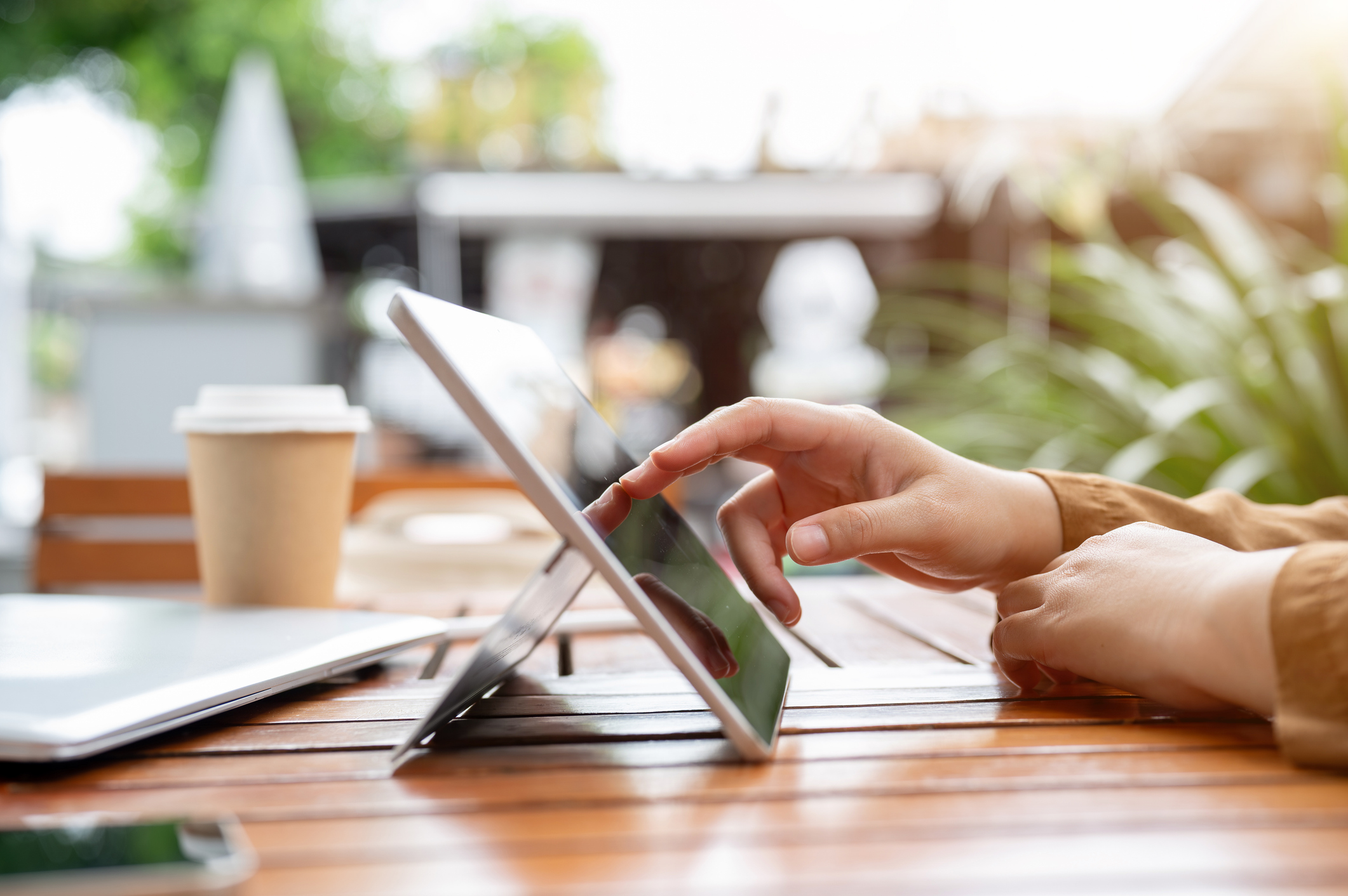 A person using a tablet at a sunlit outdoor cafe table, coffee cup nearby